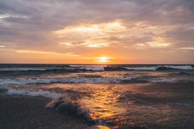 Dalgalı okyanusta güneşin batışını ve Bali 'de turuncu ve kırmızı parlaklıklarla suya yansımasını hayret verici bir manzara.