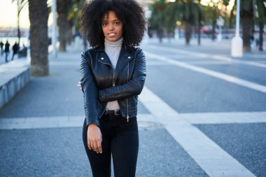 Ciddi bir Afro-Amerikalı kadın şık giyinmiş sokakta dikilip şehirde yürüdükten sonra dinlenirken kameraya bakıyor.