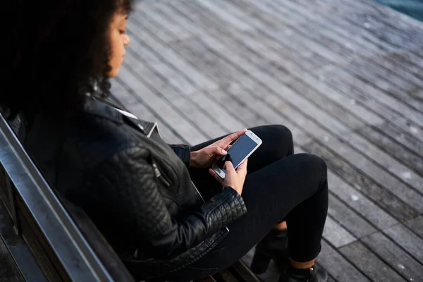 自信に満ちたアフリカ系アメリカ人女性の高い角度カジュアル服ベンチに座って路上で携帯電話でメッセージ — ストック写真