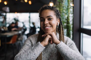 Bluetooth kulaklıklı koyu tenli bir kadının portresi kafeteryada boş zamanlarında pozitif müzik podcast 'i dinliyor kulaklıklarıyla kameraya gülümseyen mutlu nesil Z