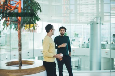 Modern ofis binasında kahve fincanlarıyla dinlenen ve iş konularını tartışan kendinden emin, çok ırklı genç meslektaşlar.