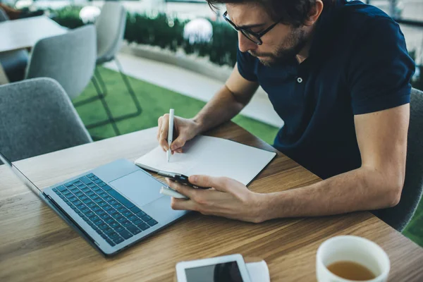 Crop Guy Eyeglasses Writing Notepad While Browsing Laptop Contemporary Workplace — Stock Photo, Image