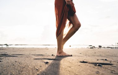 Bali 'de yanan boş okyanus kıyısının ıslak kumu boyunca yürüyen, bronzlaşmış, çıplak ayaklı bayanın yan görüntüsü.