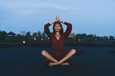 Yoga yapan sakin Asyalı kadın sabahın erken saatlerinde kumlu sahilde oturmuş vahşi doğaya karşı dinlenirken meditasyon yapıyor.