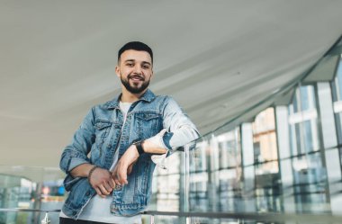 Düşük açılı, bilezik takmış bir erkek. Mola sırasında boş koridorda kameraya bakıyor.