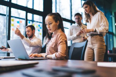 Yeni iş projeleri için strateji geliştiren bir grup düşünceli genç iş arkadaşından büyük pencereli modern çalışma alanında birlikte çalışırken...