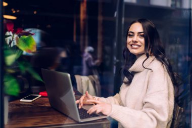 Cafe 'de bilgisayarını kullanan neşeli genç bir kadının yan görüntüsü. Bilgi analiz ederken ve tuş tuşunda yazarken uzaktan çalışmak için.