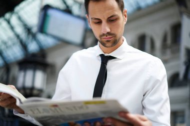 Resmi olarak odaklanmış erkek müdürün düşük açısı istasyonda durup treni beklerken gazete okumaktan zevk alıyor.