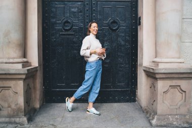 Heyecanlı turist kızın uzun bir portresi antik bir binanın yakınında inanılmaz kapıları olan, modern cep telefonuyla gezen ve kaçarken kameraya gülümseyen neşeli bir bayan gezgin.