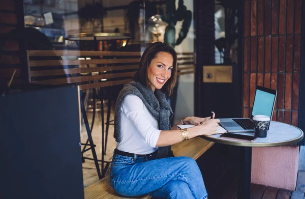 Uśmiechnięta Letnia Kobieta Robi Notatki Copybooku Siedząc Kawiarni Świeżym Powietrzu — Zdjęcie stockowe