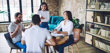 Ahşap masanın etrafında toplanıp yaratıcı iş yerinde yeni bir girişimi tartışırken aynı kıyafetleri içinde gülümseyen bir grup genç meslektaşım.