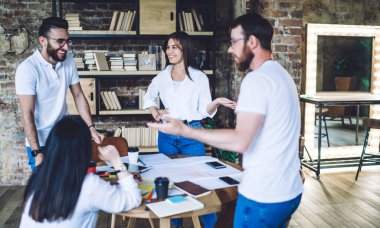 Masanın etrafında toplanan, yaratıcı fikirleri paylaşan ve rahat çalışma ortamında gülen bir grup pozitif genç meslektaşım var.