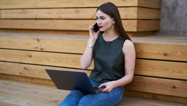 Diz üstü bilgisayarlı kız öğrencinin sokakta cep telefonuyla öğrenme ve konuşma için 4G bağlantısını kullanması, 20 'li yaşlarda düşünceli hippi bir kızın cep telefonuyla arama yapması ve uzaktan çalışması.