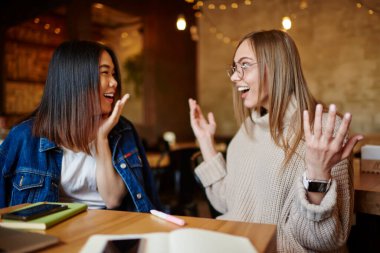 İyimser bir kadın, ağzı açık, elleri açık, birlikte boş zaman geçirirken mutlu Asyalı bir kadınla sohbet ediyor.