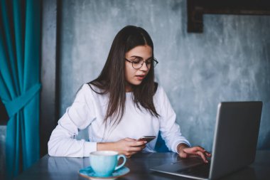 Kafede çalışırken cep telefonunda daktilo yazan, beyaz günlük giysiler içinde, ciddi bir kadın uzaktan çalışan.