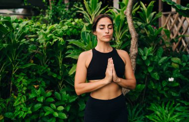 Siyah spor giysili güzel kadın yogi sabah meditasyonu sırasında hatha egzersizi namaste pozu veren çekici bir kadın iç huzuru buluyor ve ruh uyumunu hissediyor sağlıklı yaşam tarzını koruyor.