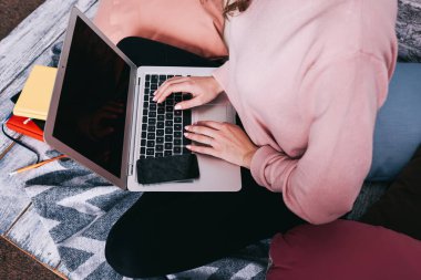 Yüzü olmayan, serbest giyinmiş, bacak bacak üstüne atmış bir kadın, dizüstü bilgisayarla proje üzerinde çalışıyor.