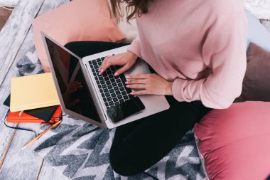 Yüksek ekin açılı, tanınmayan, günlük giysiler içinde bacak bacak üstüne atmış bir kadın dizüstü bilgisayarda yeni proje için bilgi topluyor.