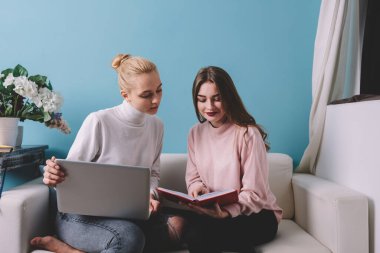 Dizüstü bilgisayarını açıp rahat bir koltukta oturup birlikte çalışırken iş arkadaşının not defterine bakan serbest çalışan bir kadın.