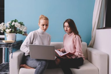 Genç bayan uzaktan kumandalı işçiler, gündelik giysiler içinde kanepede oturup proje üzerinde çalışırken bilgisayar ekranlarına bakıyorlar.