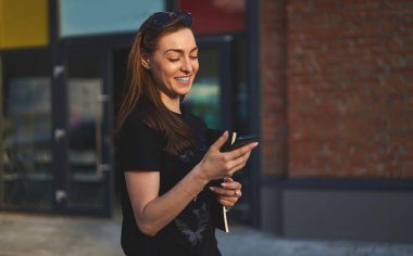 Neşeli kadın blogcu internetteki mesajlaşmalar ve sohbetler için modern cep telefonunu kullanıyor, akıllı telefon ve eğitim çizim defteri tutan sıradan giyinmiş mutlu hippi kız kablosuz internet sitesini tarıyor.