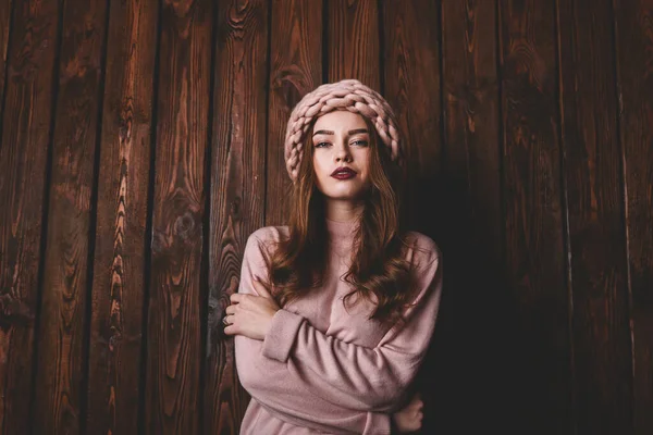 木製の壁の近くに立っている間 カメラと折り畳み式の手を見て帽子と長い髪を持つカジュアルな服装で魅力的な女性 — ストック写真