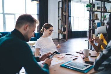 Bir grup farklı meslektaş masada oturup iş fikirlerini tartışırken akıllı telefonları karıştırıyor ve aydınlık odada kahve içiyor.