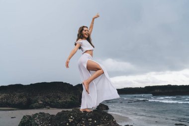 Kumlu kumsalda yaz tatilinin tadını çıkartırken gülümseyen ve bakışlarını kaçıran iyimser kadın gezginin yan görüntüsü.