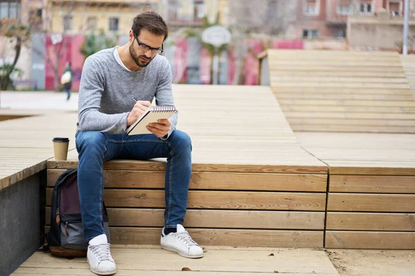 Concentrated Bearded Male Casual Clothes Eyeglasses Sitting Wooden Podium Writing — Stock Photo, Image