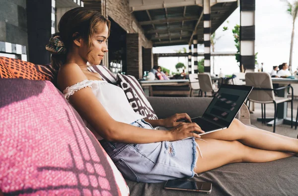 Netbook ve cep telefonuyla rahat koltukta oturan ve tropikal tatil boyunca çalışan serbest çalışan kadın.