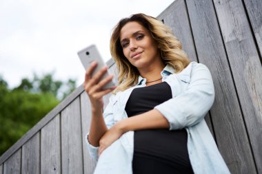 Açık havada poz veren gündelik giyinmiş kadın blog yazarının yarım boy portresi. Şehirde internet ağı kurmak için akıllı telefon teknolojisini kullanan beyaz bir kız.