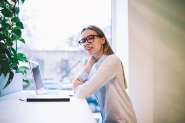 Cafe 'de bilgisayarında bitkilerle çalışırken kameraya bakan şık elbiseli ve gözlüklü kadının yan görüntüsü.