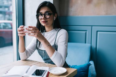Uzun saçlı, sıradan giyinmiş, gözlüklü, kahve içen ve gününü kafede defterle geçirip, akıllı telefondan müzik dinleyerek geçiren zarif bir bayan.