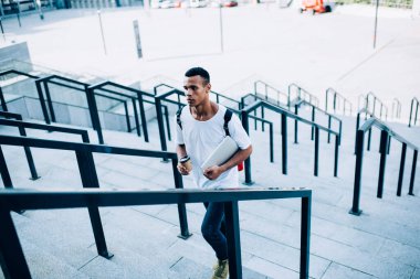 Beyaz tişörtlü, kot pantolonlu, kendine güvenen genç Afrikalı Amerikalı bir adamdan kahve ve üst katta yürürken modern bir dizüstü bilgisayar taşıyordu.