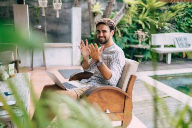 Yazın göletin yanında dizlerinin üzerinde netbook ile oturan ve kameraya bakan gündelik giyinen pozitif erkek uzaktan kumandalı işçinin yan görüntüsü