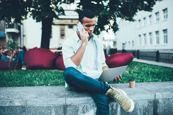 Homem Afro Americano Pensivo Usando Telefone Celular Enquanto Digita Netbook — Fotografia de Stock