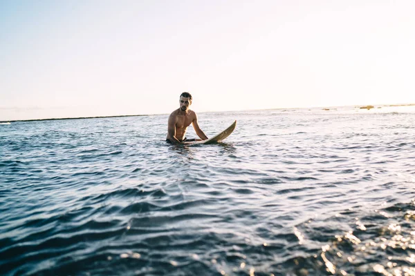 年轻的裸体男冲浪手 坐在海上的短板上 在夕阳西下飘浮后 一边回头 一边回头看一边翻看 — 图库照片