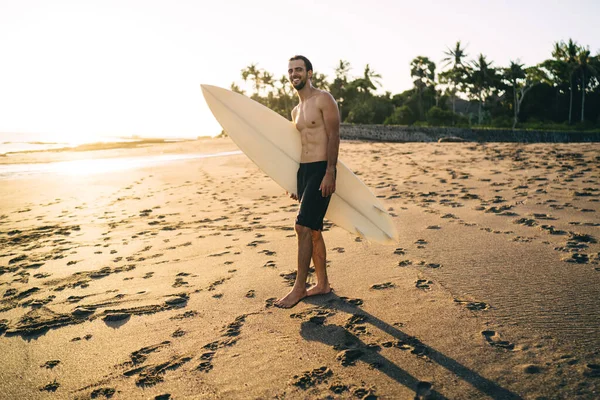 Pełna Długość Wesoły Człowiek Profesjonalną Deską Surfingową Uśmiecha Się Kamery — Zdjęcie stockowe