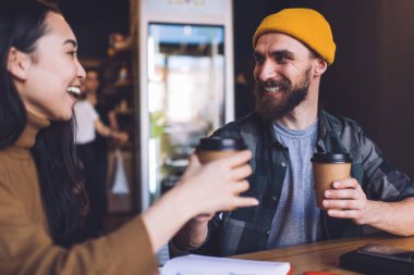 Kahve molası sırasında, kafenin içindeki organizasyon planlamasından memnun olan başarılı erkek ve kadın arkadaşlar ellerinde hazır fincanlar ve kahkahalar tutan neşeli hipster öğrenciler.