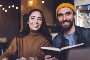 Kitapla gülümseyen genç sakallı adam kafeteryada çalışırken neşeli kız arkadaşının yanına oturmuş ve birlikte kameraya bakıyorduk.