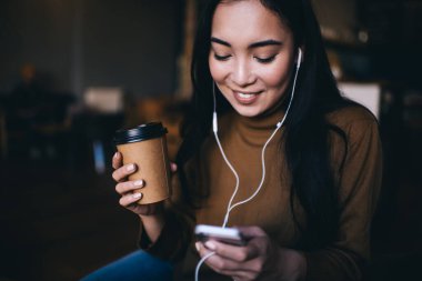 Kaygısız hippi kız mesajlaşmak ve medya uygulamasından müzik şarkıları seçmek için akıllı telefon teknolojisini kullanıyor, pozitif video yayınlarını izlemek için internet sitesine girip kahve içen mutlu kadın.