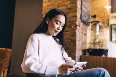 Elektronik kulaklıklı beyaz bir kadın 4G internet ve bluetooth 'a bağlanan modern dokunmatik ekranda müzik ve sosyal yayınlardan hoşlanan kulaklıklı bir kadın videolar izliyor.