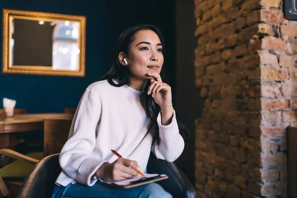 Konzentrierte Asiatische Schriftstellerin Freizeitkleidung Mit Echten Drahtlosen Kopfhörern Und Notizen — Stockfoto