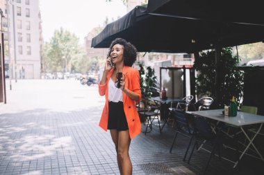 İyimser, turuncu ceketli, güneş gözlüklü genç bayan yazın sokakta konuşurken yüzünü çevirmiş gülümsüyor.