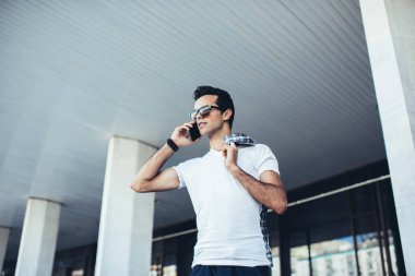 Beyaz tenli hippi, günlük kıyafetler giyip uluslararası sohbet için kablosuz bağlantı kuruyor. Moda güneş gözlüklü milenyum turisti mobil uygulama üzerinden arıyor.