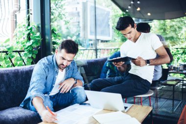 Kafkasyalı erkek bilişim uzmanları, sokak kafeteryasında uzaktan işbirliği yaparken evrak işlerini inceliyor, modern laptop teknolojisi ile yetenekli genç bir öğrenci ve birlikte sınavlara hazırlanıyor.