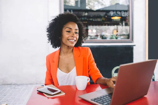 穿着休闲装的满意的非洲裔美国女士在现代自助餐厅边喝咖啡边上网查社交媒体 — 图库照片