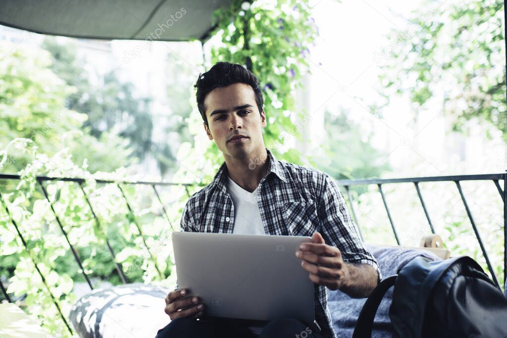 Portrait of Caucasian male programmer with laptop technology looking at camera while working remotely at cafe terrace, skilled man with digital netbook posing outdoors keeping freelance lifestyle