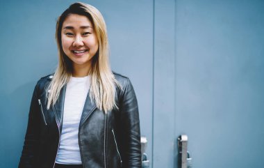 Modaya uygun deri ceket giyen neşeli Asyalı hippi kızın yarım boy portresi. Kameraya gülümseyen, şık giyinmiş, şehir ortamında poz veren mutlu Çinli kadın. Eğlencenin tadını çıkarıyor.