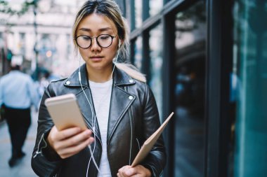 Optik gözlüklü Çinli hippi kız ve mobil teknolojiye indirmek için müzik seçen elektronik kulaklıklı, eğitim kitaplarında radyo dinleyen ve ağda mesajlaşan bin yıllık kadın.